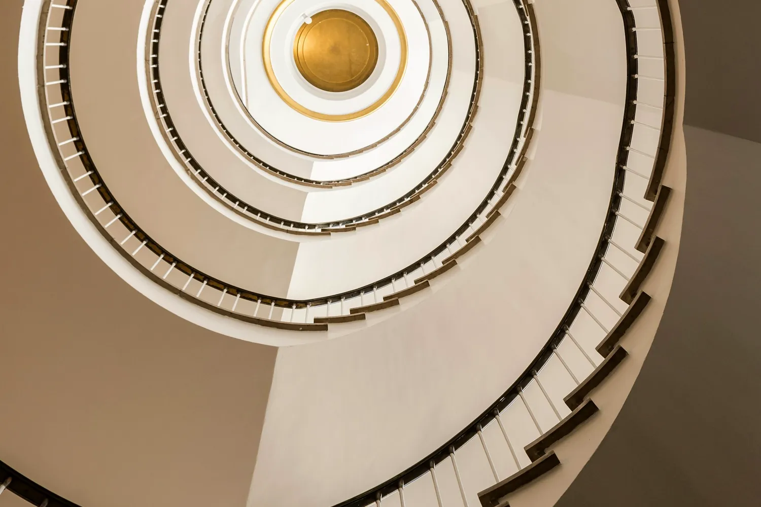Un escalier en colimaçon blanc photographié d'en bas, avec un puits de lumière au centre
